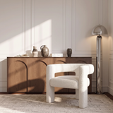Fauteuil CELIA en tissu bouclette crème dans un salon parisien à moulures, devant un buffet en bois et un lampadaire chromé, Sia Deco