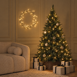 Sapin de Noël lumineux Fluffy vert 180 cm allumé dans un salon avec cadeaux et couronne lumineuse