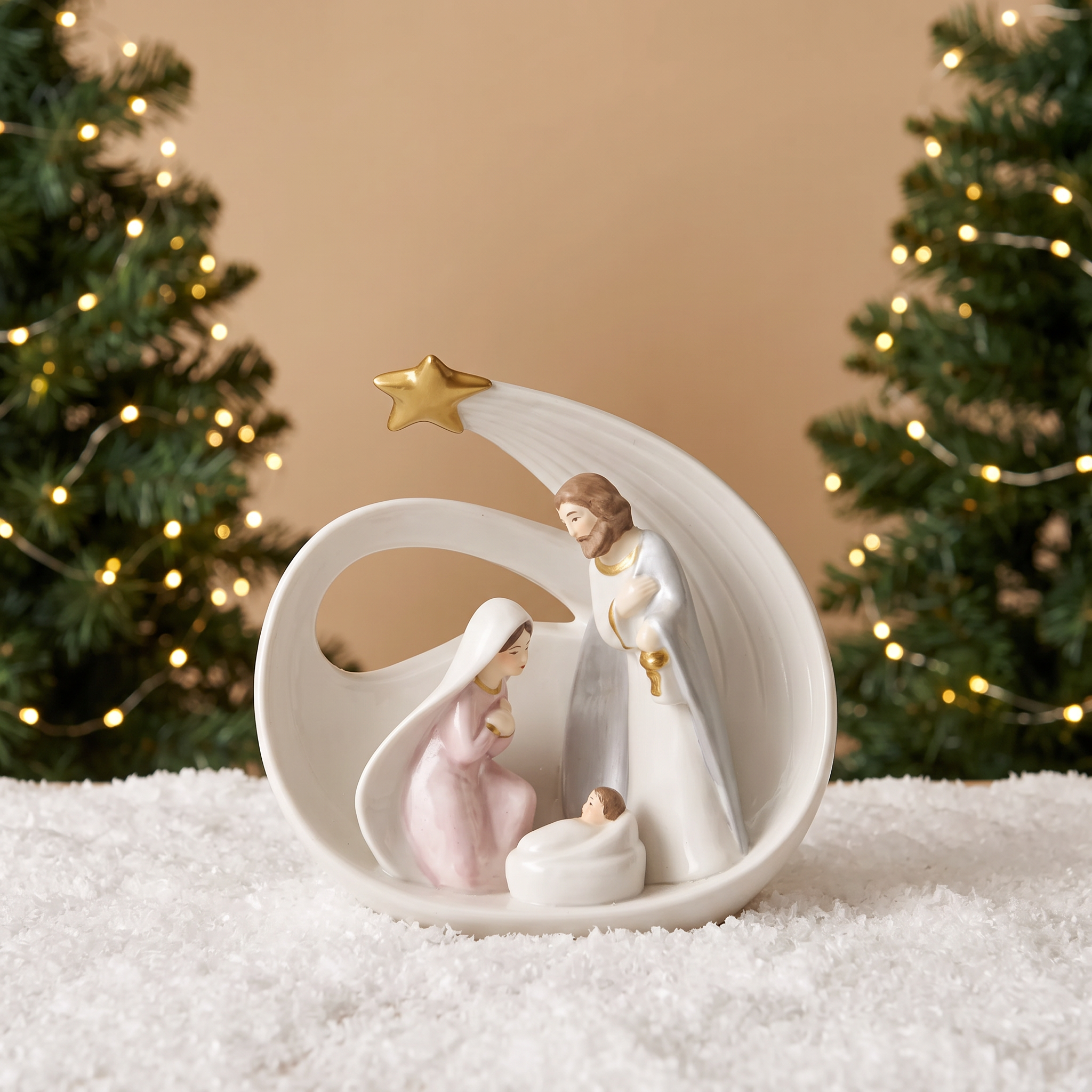 Crèche de Noël Bethléem en porcelaine blanche et dorée, posée sur la neige devant un sapin de Noël lumineux flouté