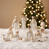 Crèche de Noël Céleste en porcelaine, set de 11 figurines disposées sur la neige devant un sapin lumineux flouté